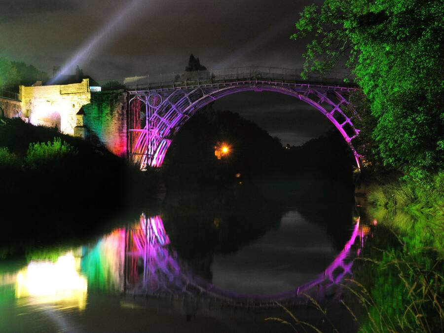 A bridge with a reflection in the water, surrounded by greenery.