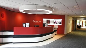 Uma área de recepção com esquema de cores vermelho e branco, uma luminária circular sobre o balcão de recepção e um relógio na parede.