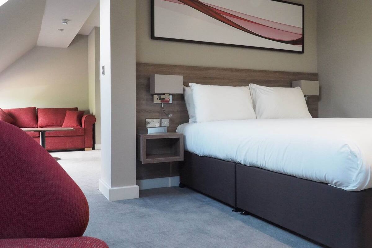 Une chambre d’hôtel moderne avec un grand lit, un canapé rouge et un tableau abstrait accroché au mur.