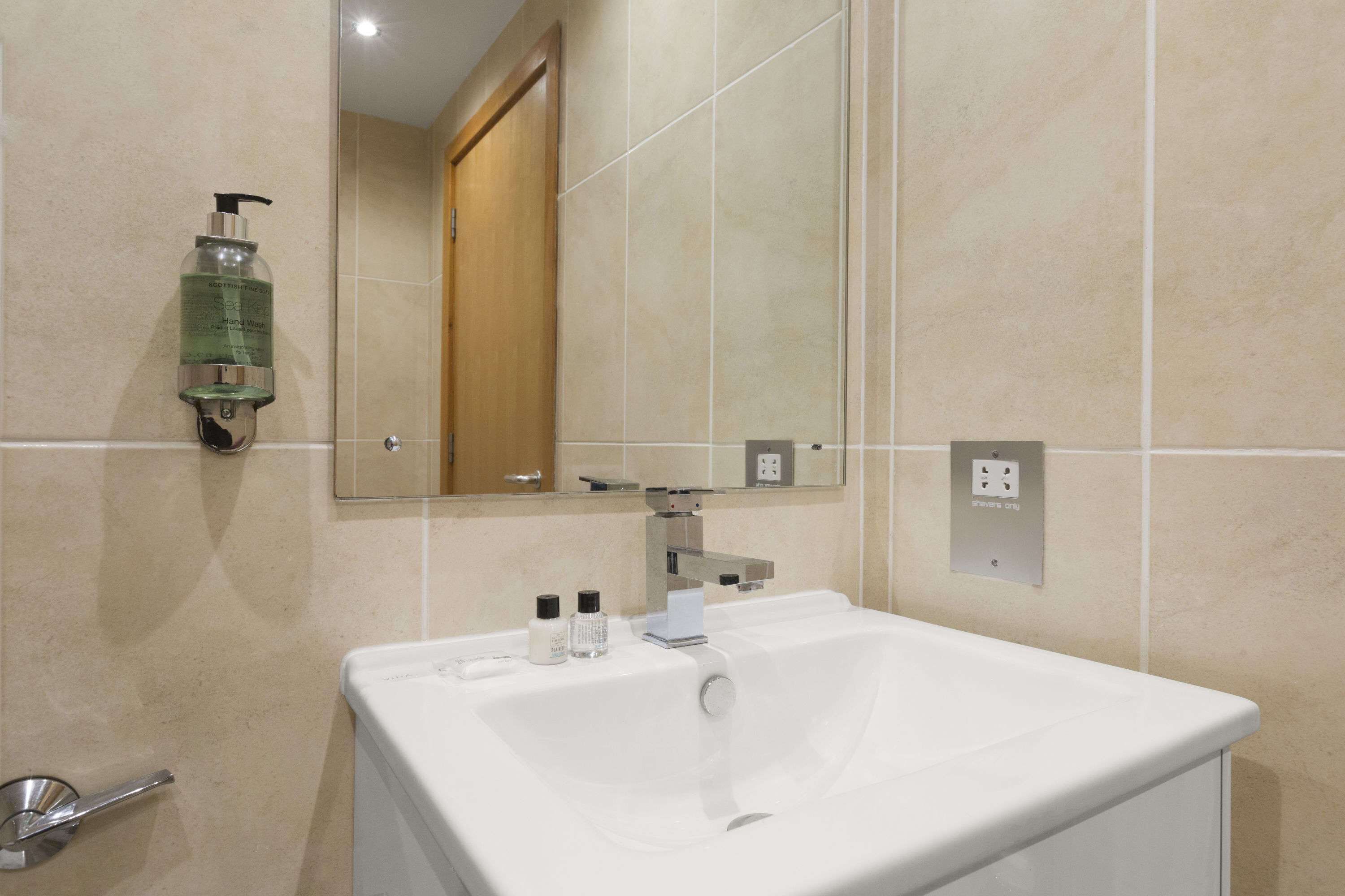 A bathroom with a white sink, a mirror, and a hand soap dispenser on the wall.