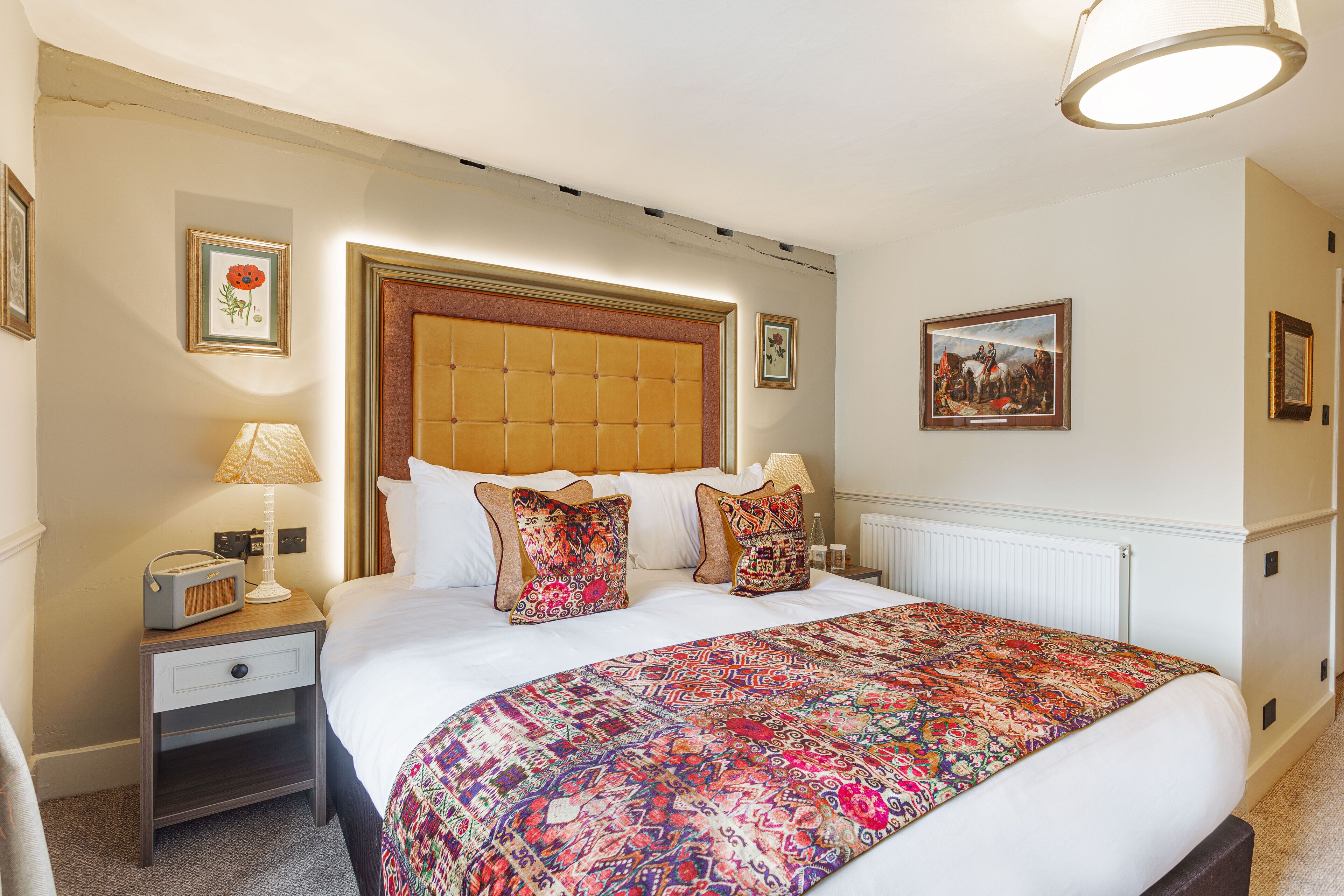 A hotel room with a large bed, a nightstand with a lamp, and a framed picture on the wall.