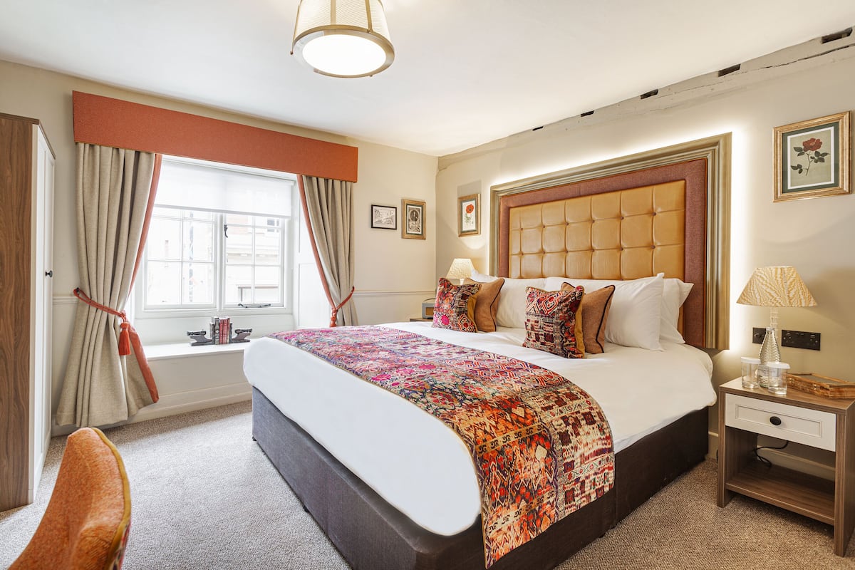 A hotel room with a large bed, a nightstand, a window with curtains, and a view of the outside.
