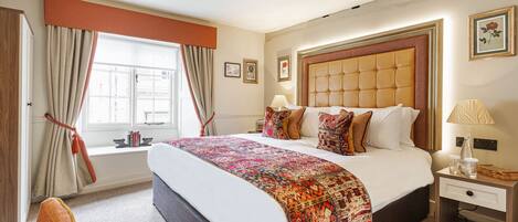 A hotel room with a large bed, a nightstand, a window with curtains, and a view of the outside.