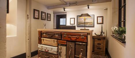 A reception area with a wooden cabinet of vintage suitcases, a reception desk, framed artwork on the walls, and a patterned carpet.