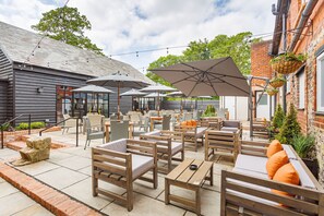 An outdoor patio area with wooden furniture, large umbrellas, and hanging flower baskets. - The George Hotel, Amesbury, Wiltshire (Salisbury)