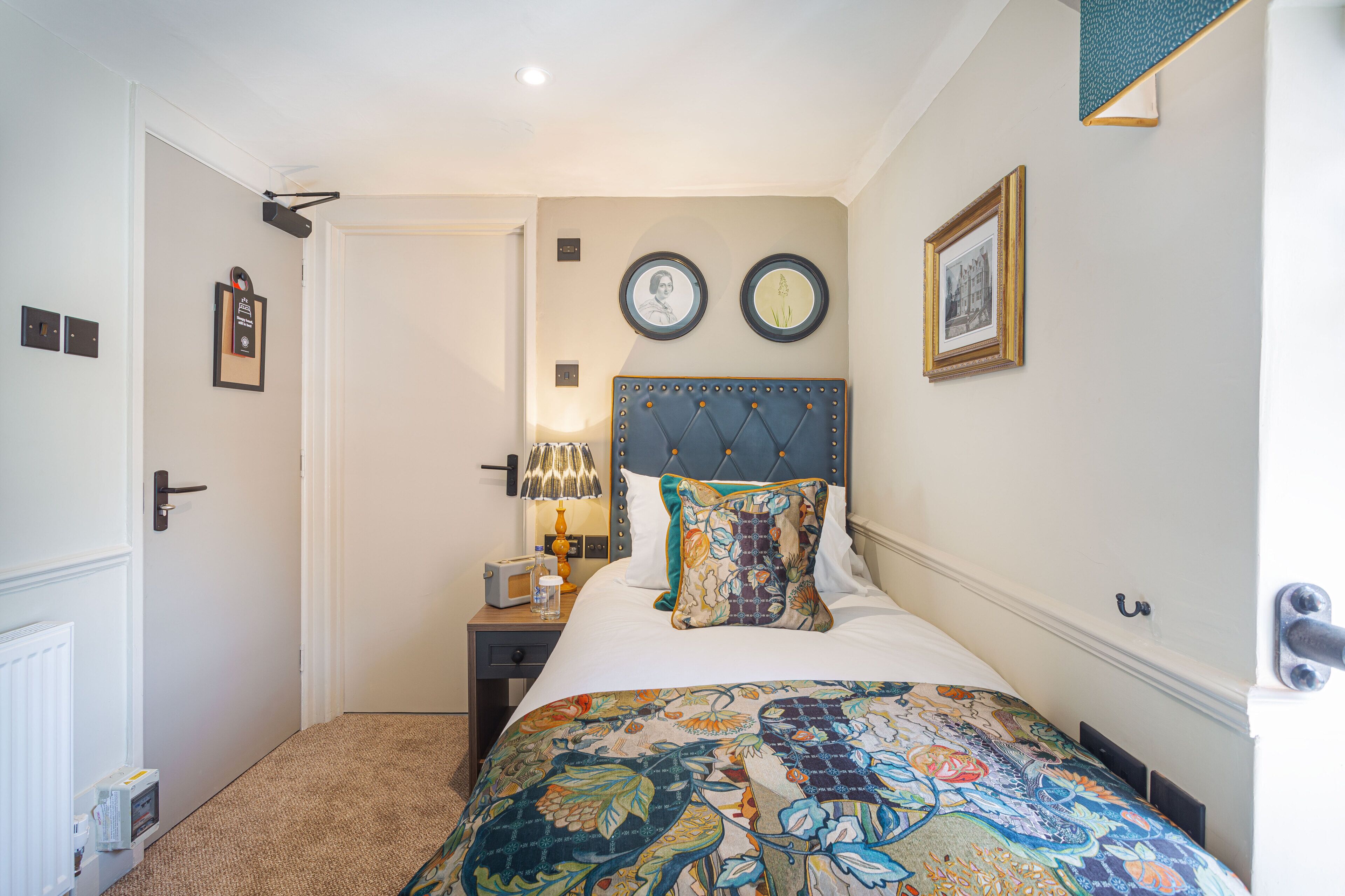 A bedroom with a bed, a nightstand, a lamp, and two framed pictures on the wall.