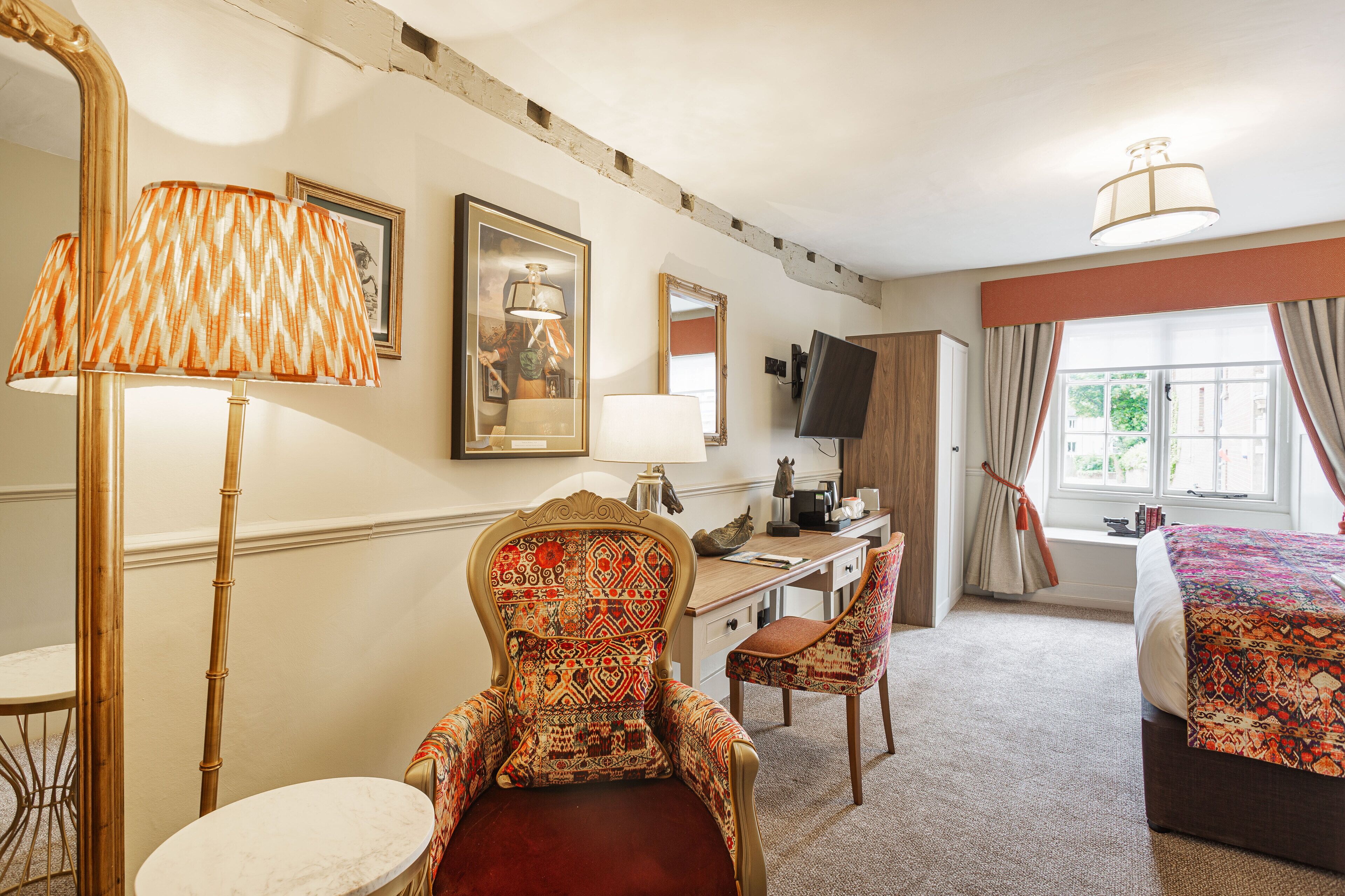 A hotel room with a bed, a desk, a chair, a large mirror, and a lamp.