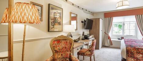 A hotel room with a bed, a desk, a chair, a large mirror, and a lamp.