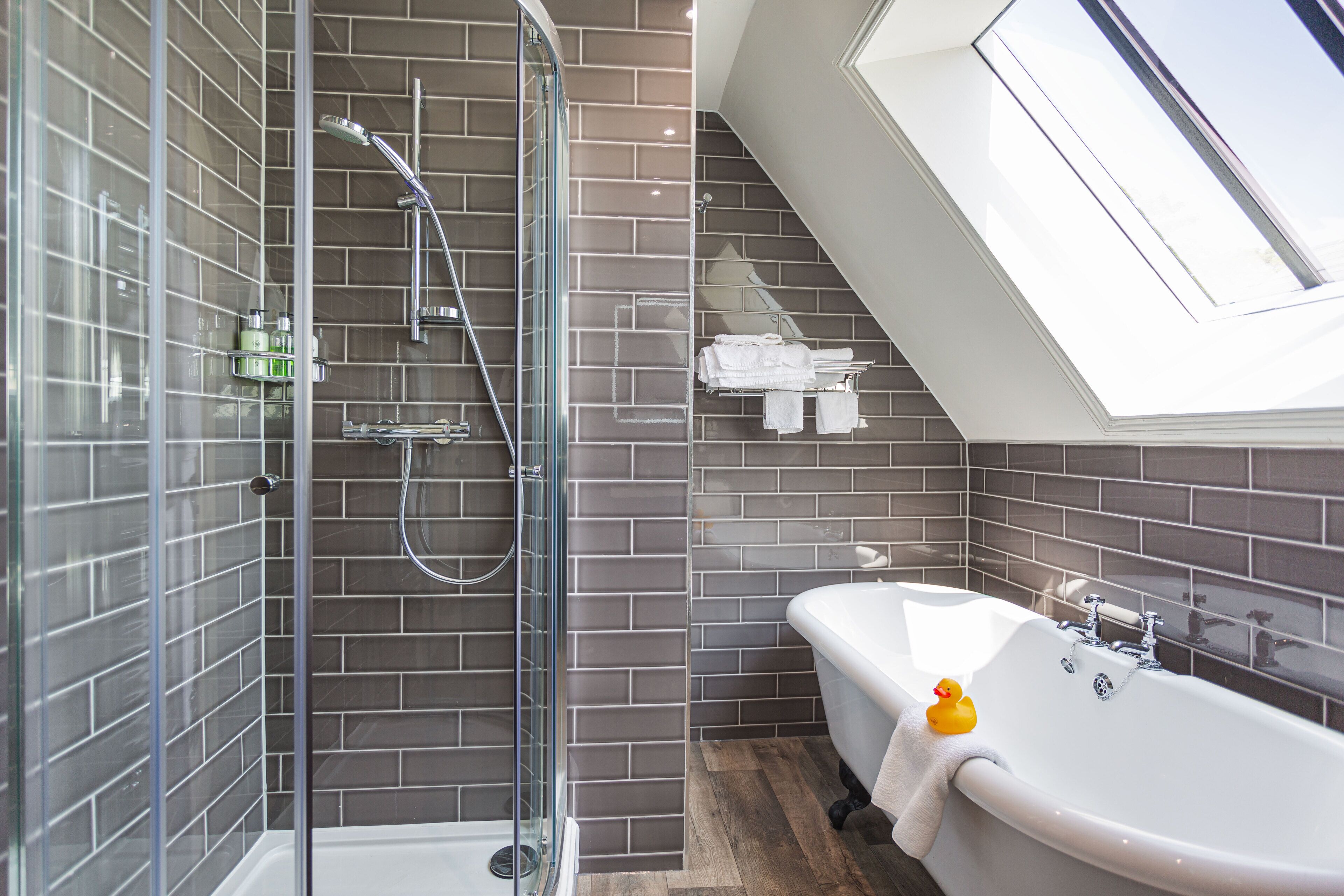 A modern bathroom with a glass-enclosed shower, a freestanding bathtub, and a skylight.
