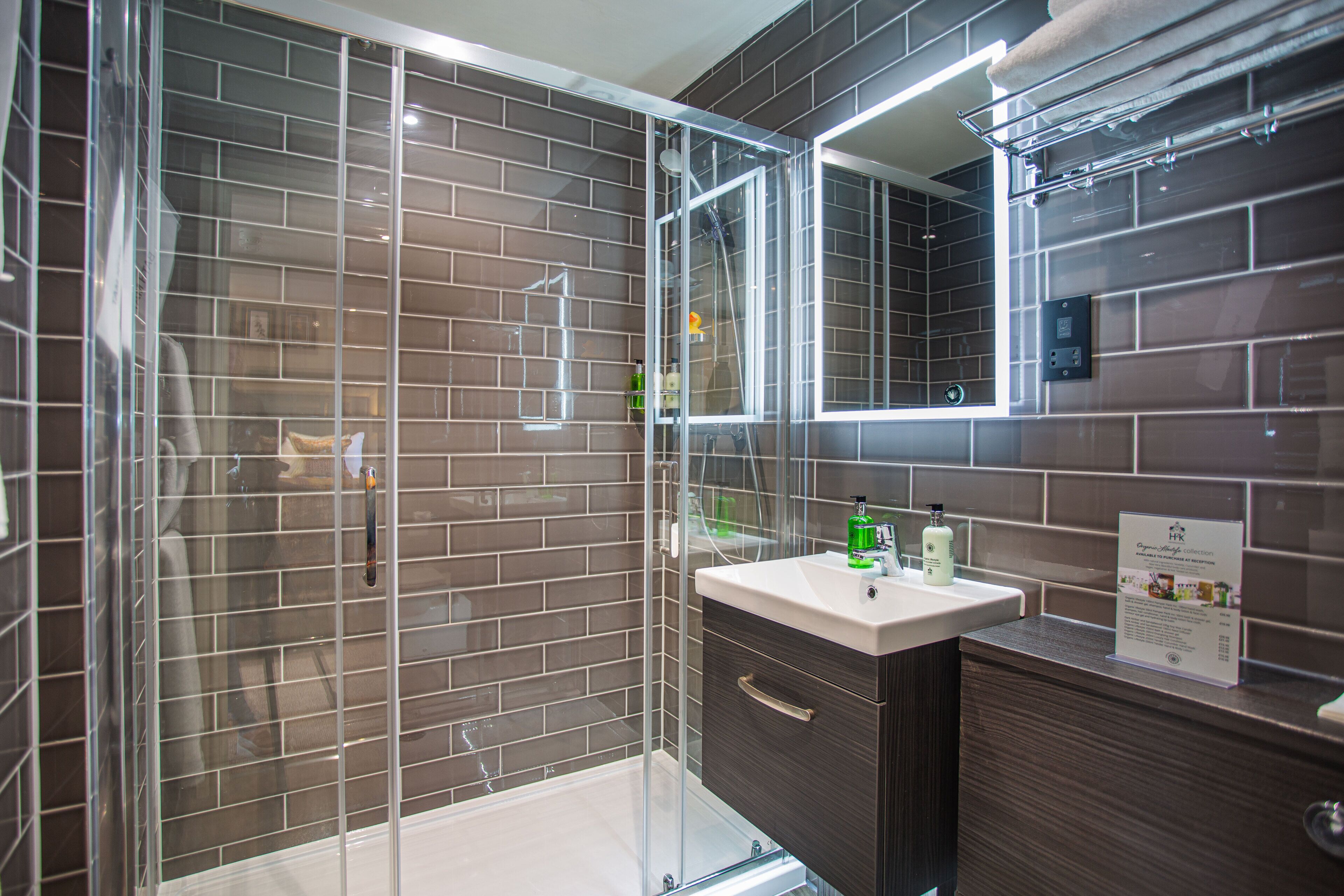 Un baño moderno con ducha de mampara de vidrio, tocador con espejo y pared de azulejos.