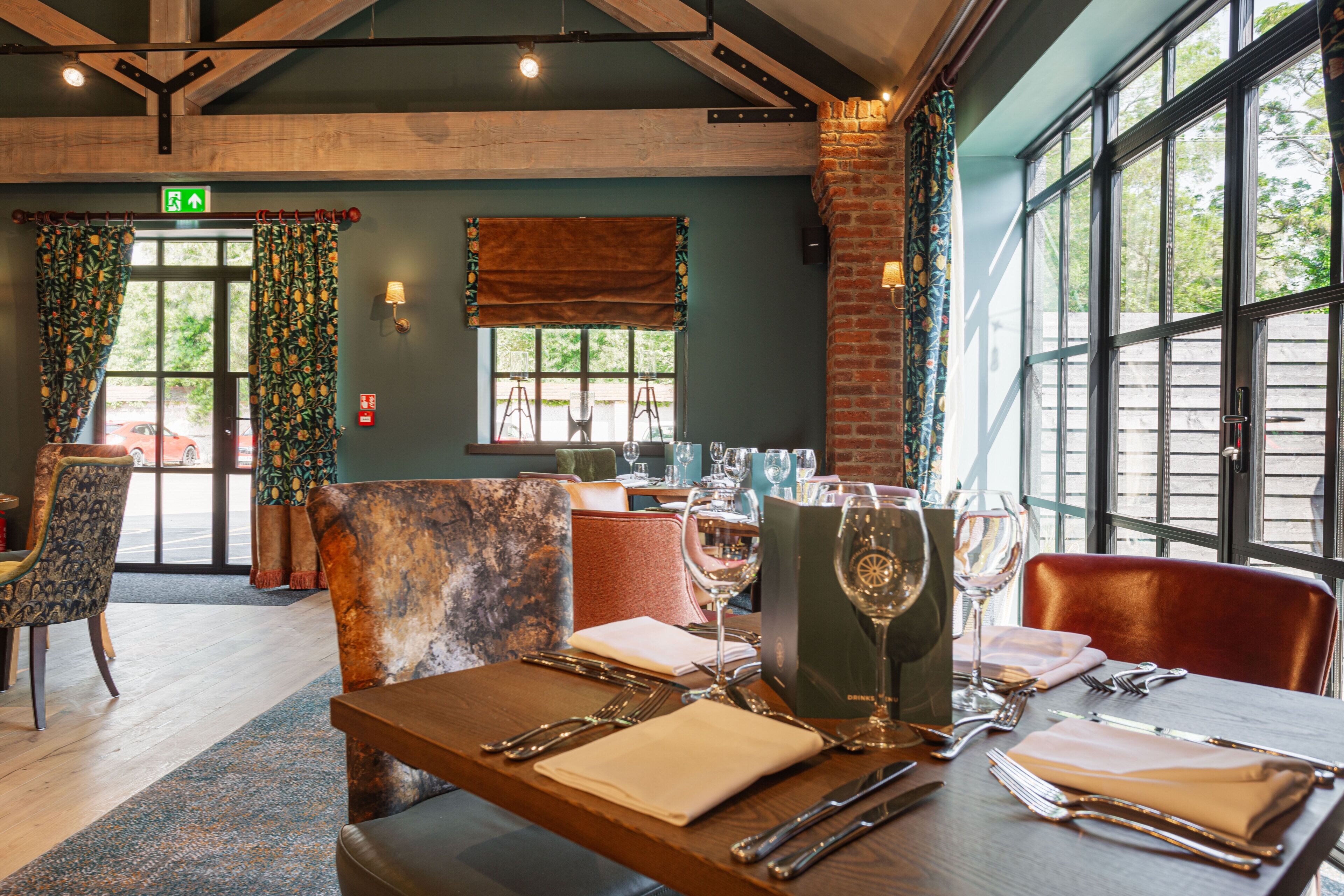 L’intérieur d’un restaurant, avec un plafond en bois, de grandes fenêtres et une table dressée pour le repas.