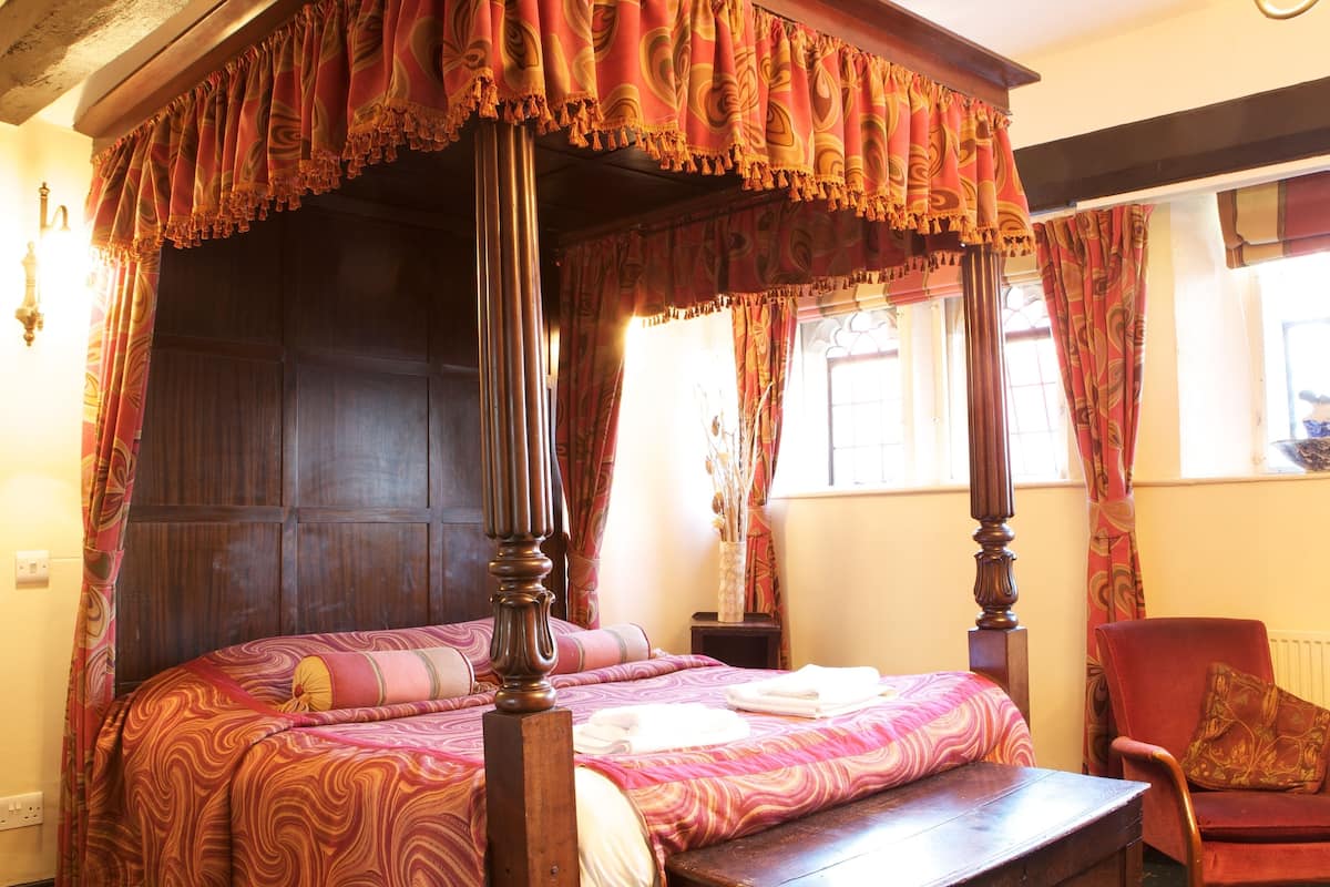 A four-poster bed with a canopy, a wooden nightstand, a chair, and a vase with dried plants.