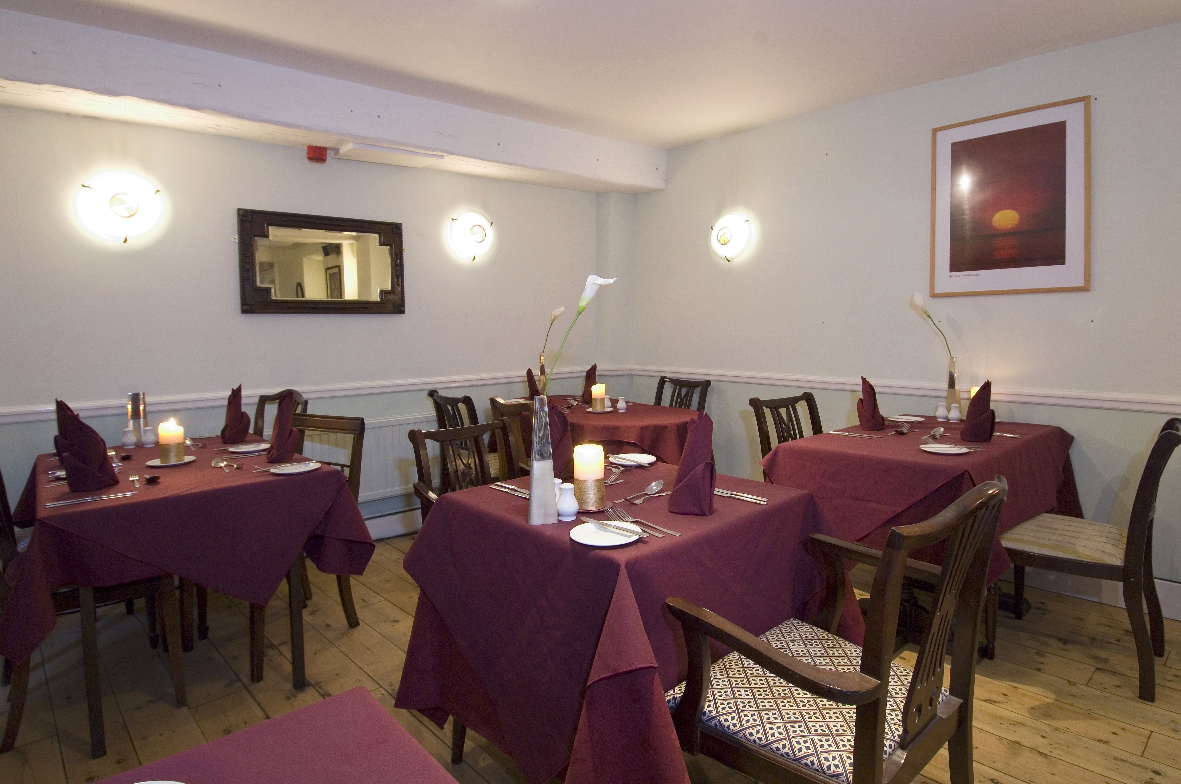 Un espace repas avec des tables dressées pour quatre personnes, chacune agrémentée d’une bougie et d’un vase de fleurs.