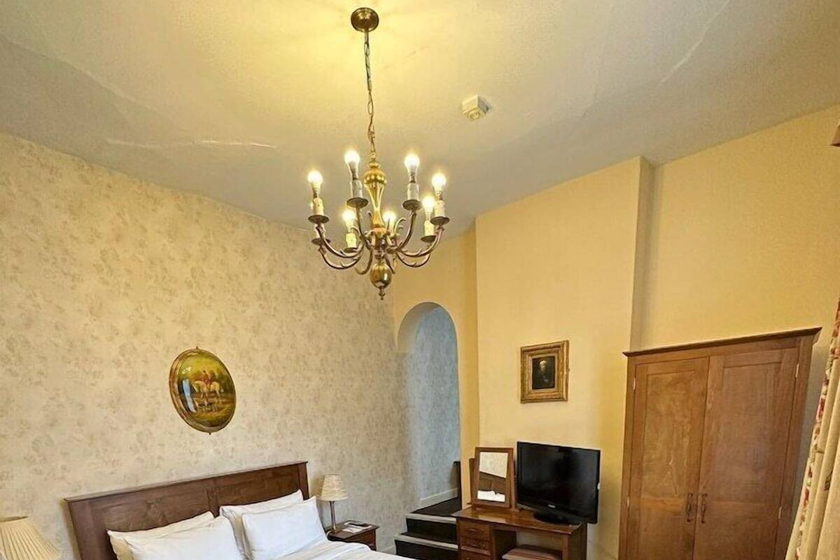 A hotel room with a large bed, a television, a wooden wardrobe, and a chandelier.