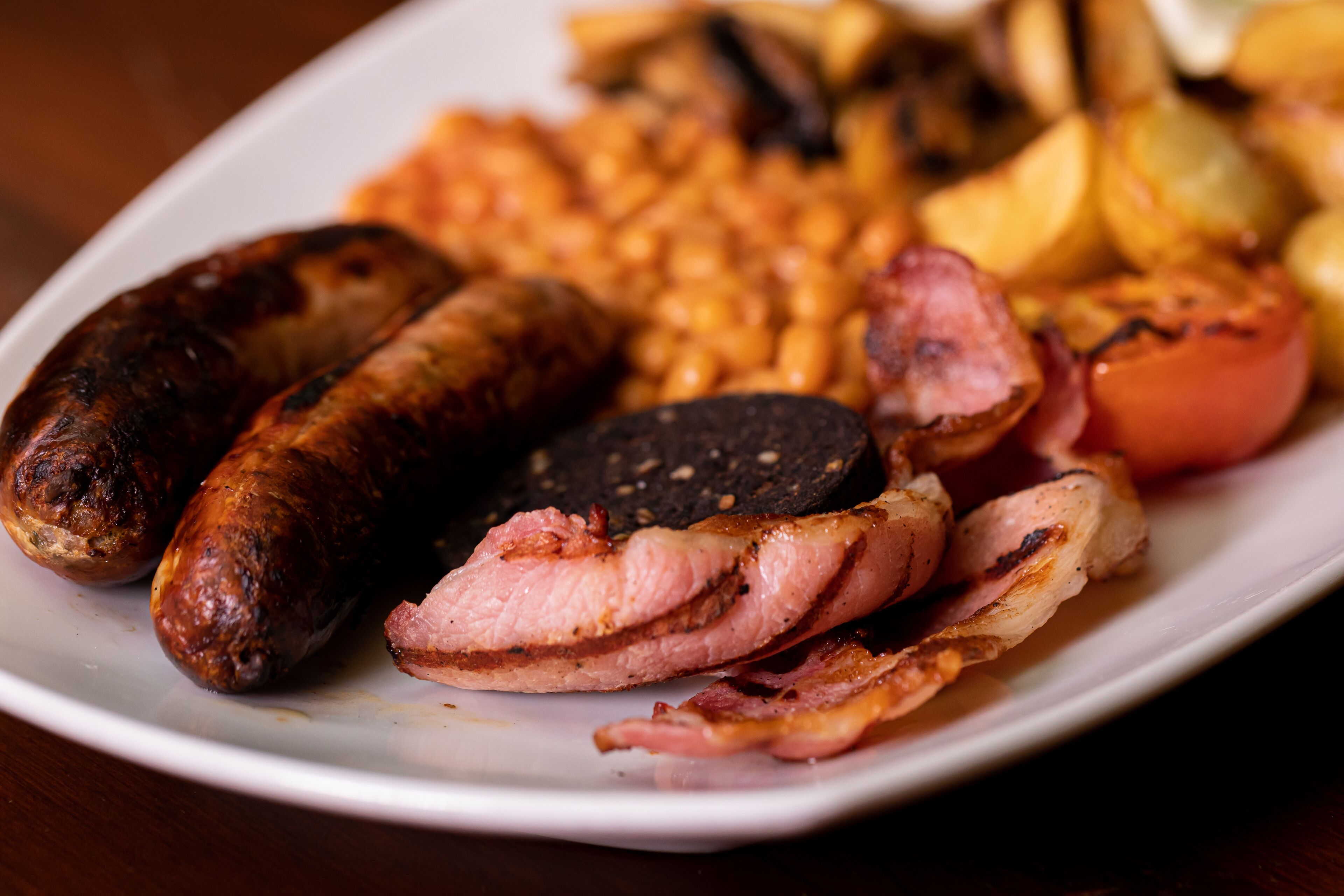 Un plato de comida con salchichas, tocino y papas asadas.