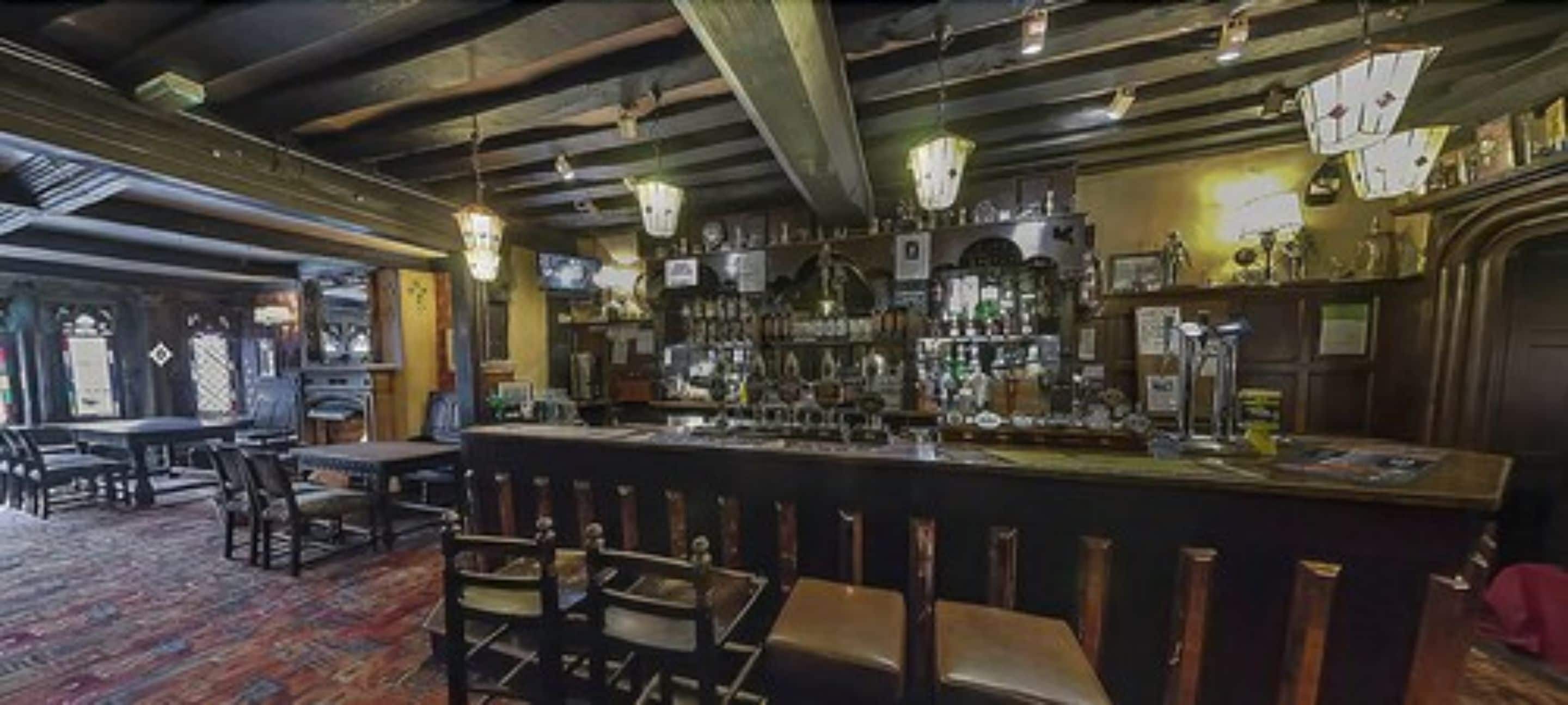 A bar area with a long counter, multiple hanging lights, and a variety of bottles and glasses.