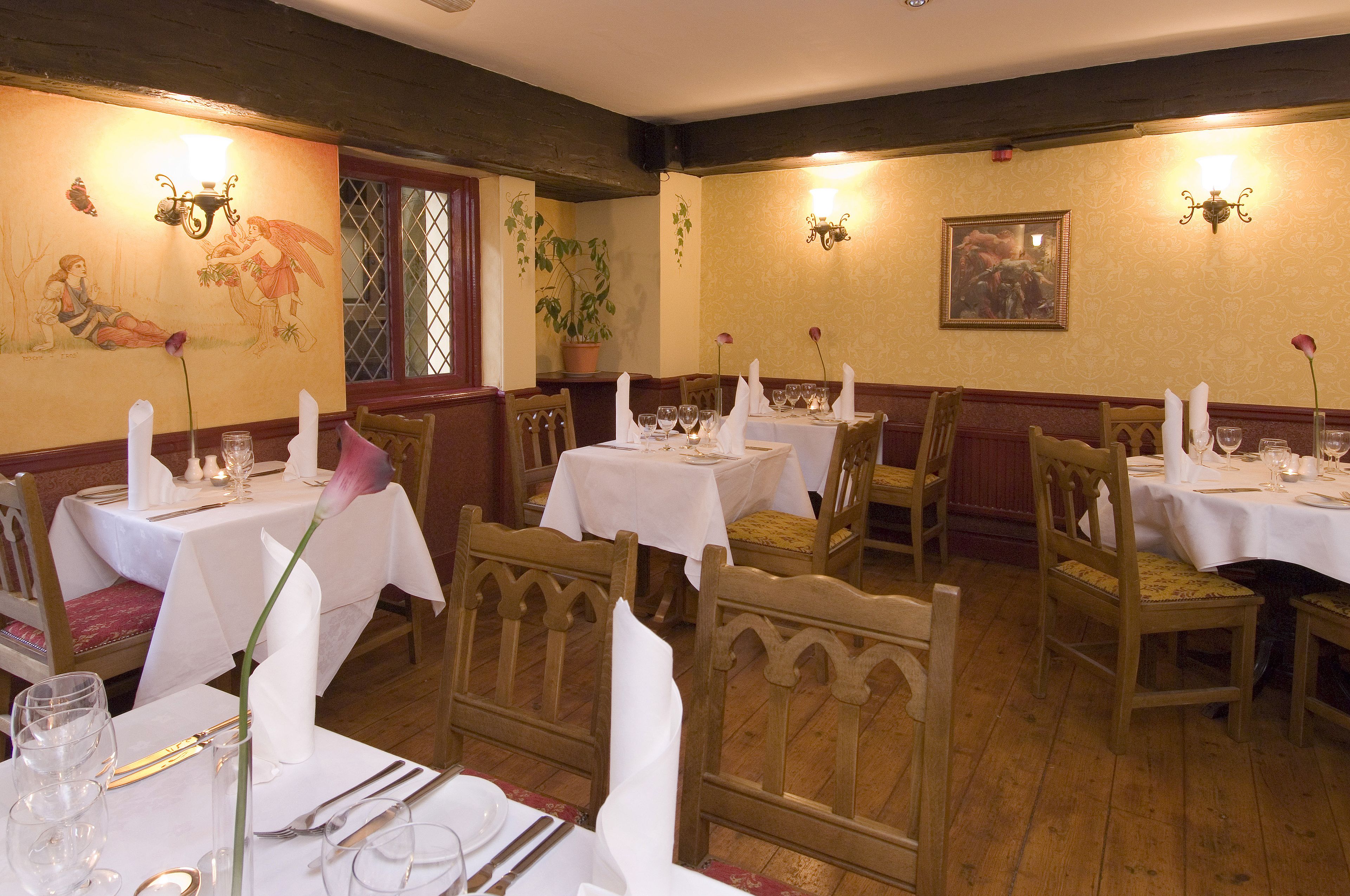 Un comedor con sillas y mesas de madera, manteles blancos y centros de mesa con velas.