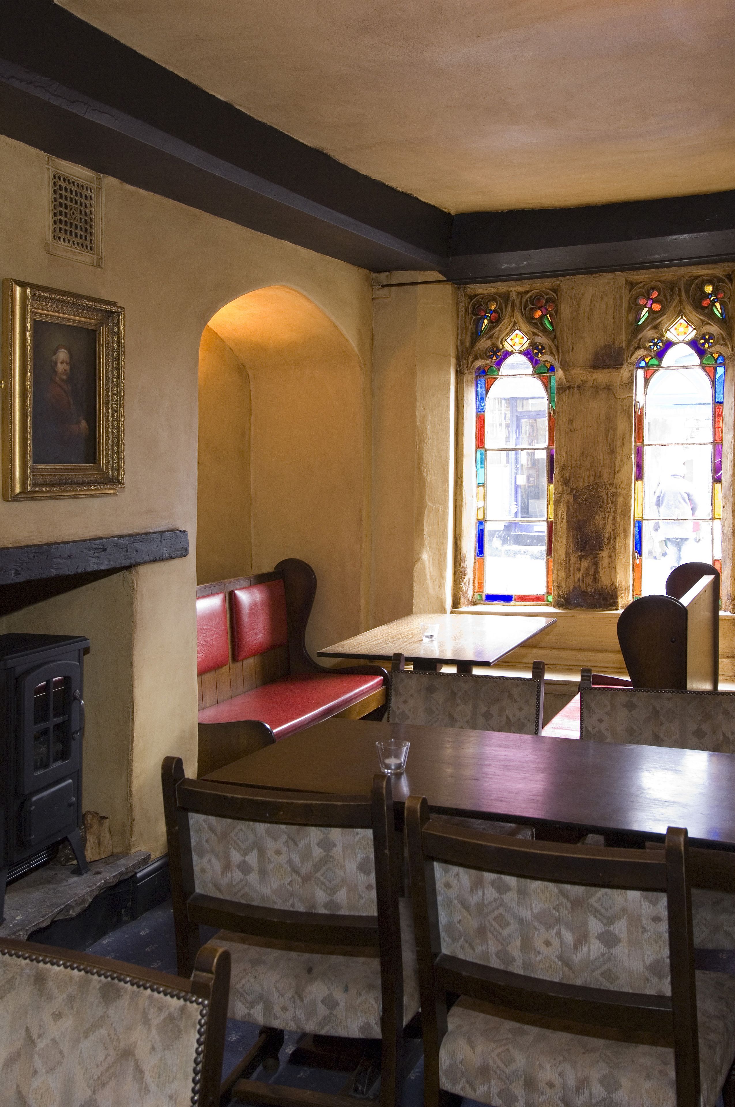 A dining area with wooden tables and benches, stained glass windows, and a fireplace.