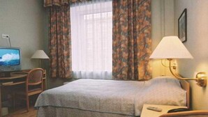 A hotel room with a bed, a desk with a computer, a lamp, and a window with curtains.