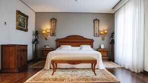 A bedroom with a wooden bed, two bedside tables, a bench, a patterned rug, and wall-mounted sconces.
