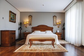 Classic bedroom with a large bed, bedside tables, and a bench, surrounded by artwork and wall sconces.