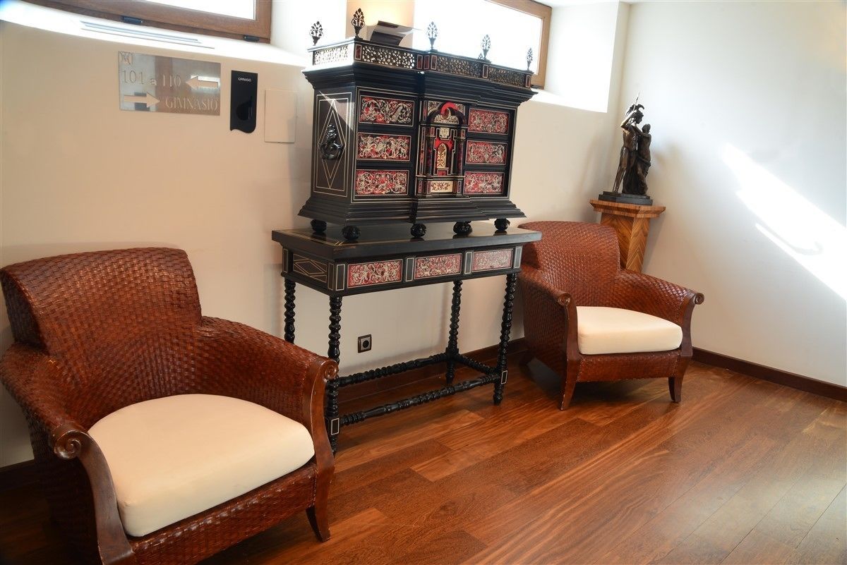 Une pièce comprenant deux fauteuils en osier, un buffet en bois foncé orné de motifs complexes et une statue posée sur un piédestal.