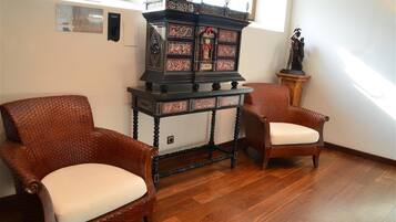 Une pièce comprenant deux fauteuils en osier, un buffet en bois foncé orné de motifs complexes et une statue posée sur un piédestal.