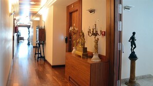 A hallway with wooden flooring, a reception desk with a wooden finish, and a statue on the right.
