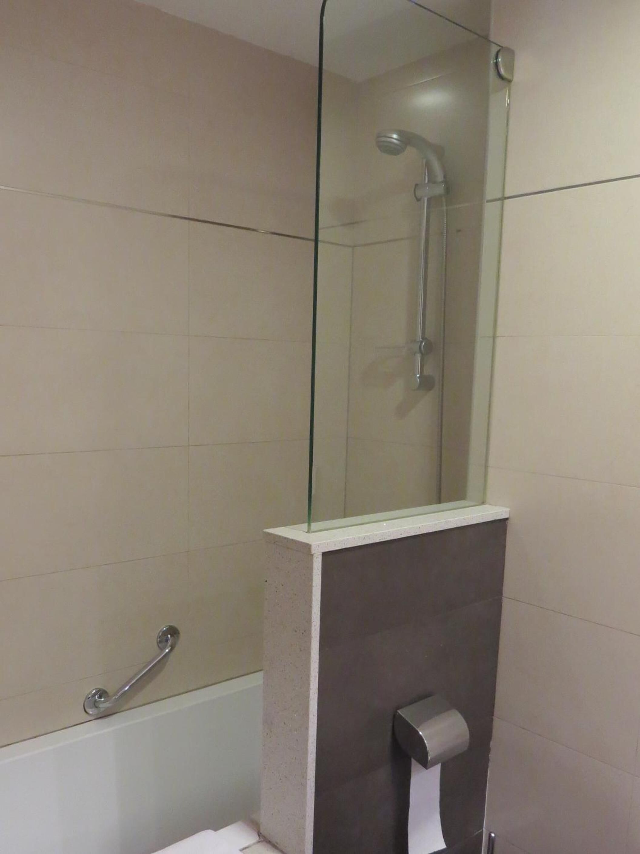 A bathroom with a glass-enclosed shower, a toilet, and a paper towel dispenser.