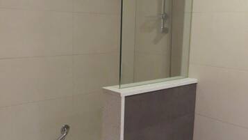 A bathroom with a glass-enclosed shower, a toilet, and a paper towel dispenser.