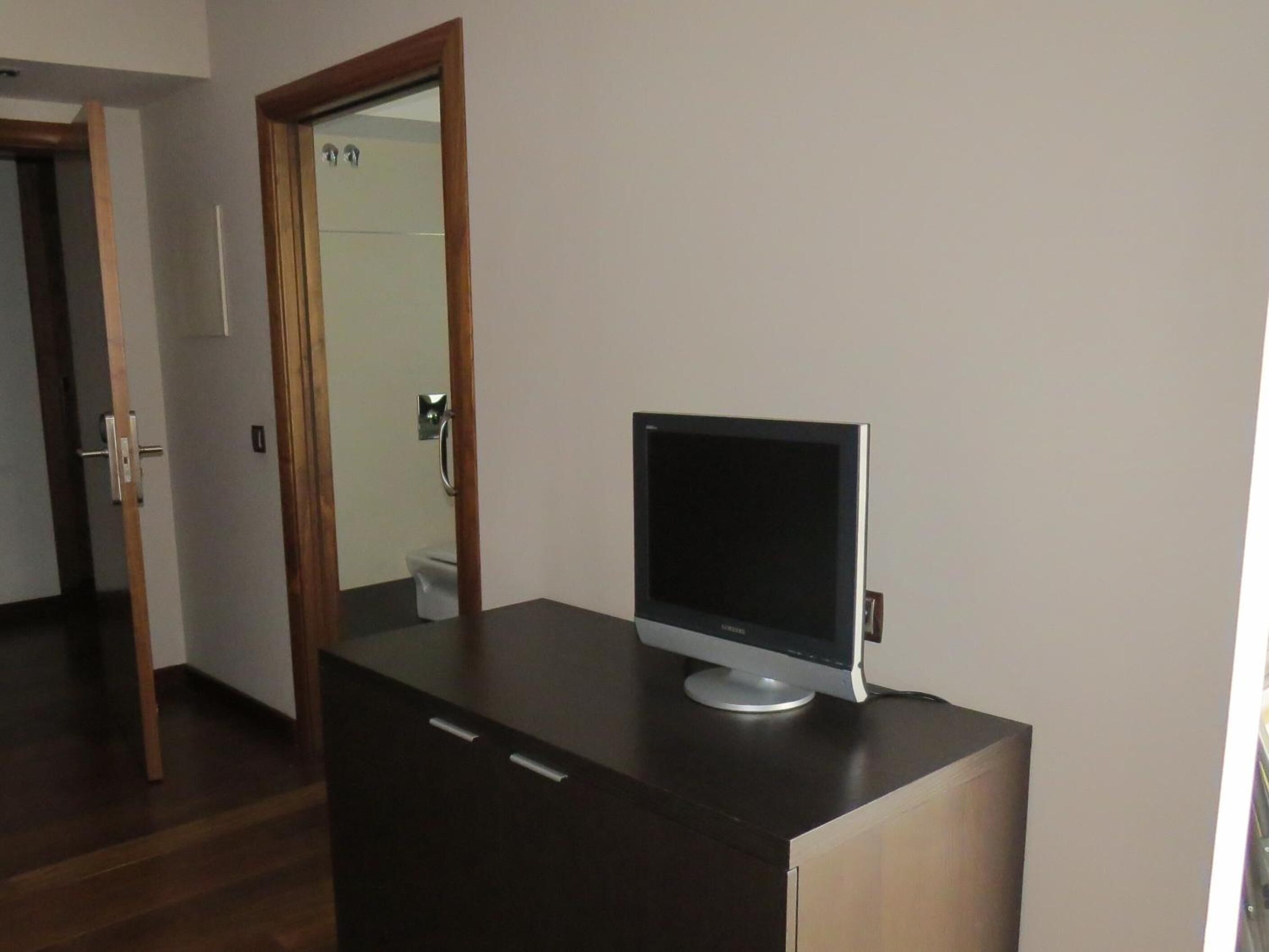 Een kamer met een donker houten bureau, een flatscreen televisie en een spiegel aan de muur.