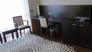 A hotel room with a bed, a desk, two chairs, a television, and a waste bin.