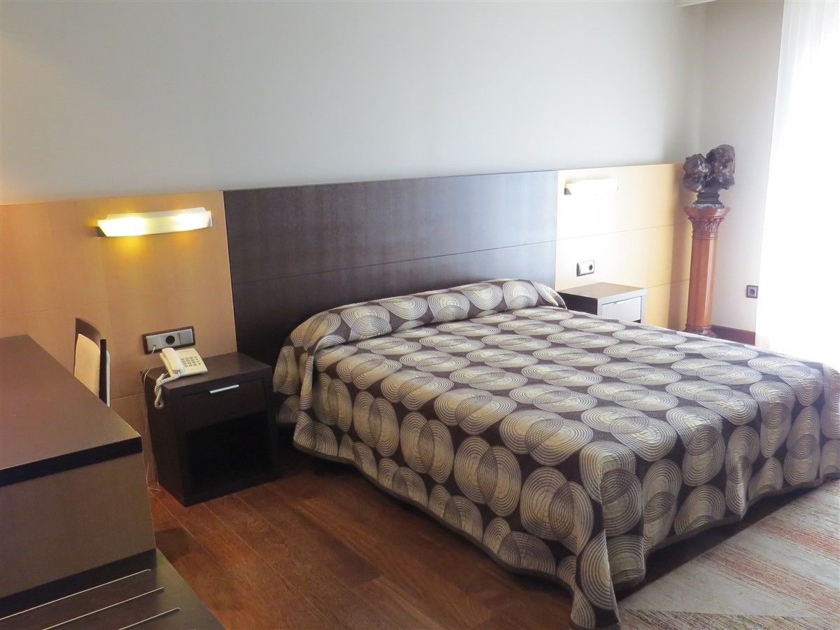 Een hotelkamer met een groot bed, een nachtkastje met een lamp, een telefoon en een bureau met een stoel.