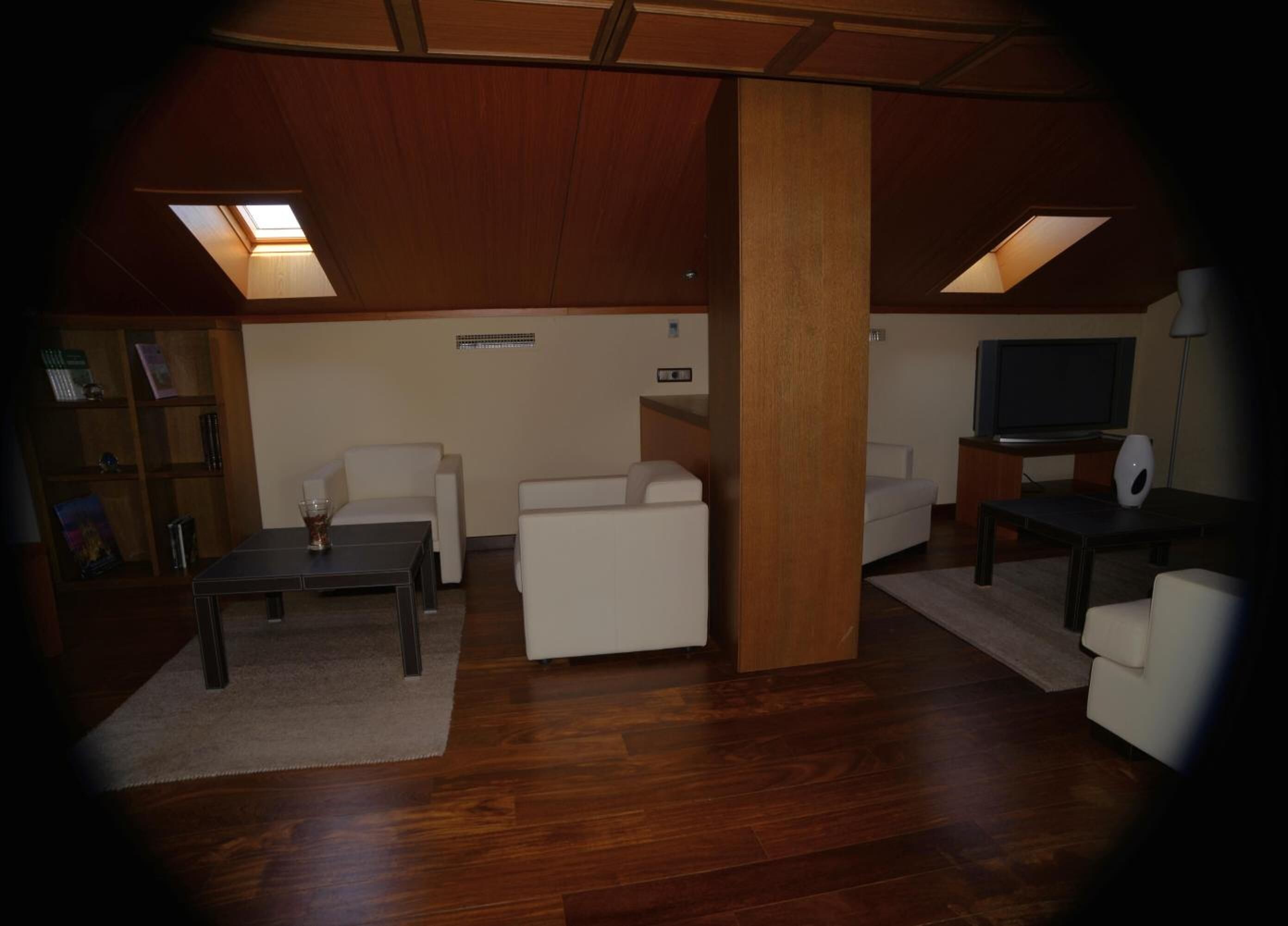 Una sala de estar con piso de madera, un sofá blanco, una mesa de centro, un televisor y una estantería.