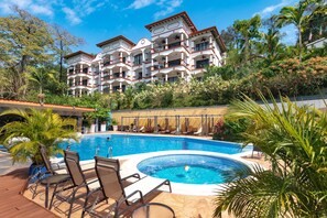 Un hotel con piscina, sillas de descanso y exuberante vegetación tropical.