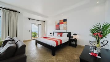 A hotel room with a bed, a sofa, a nightstand, a lamp, a vase with flowers, and a view of the outdoors.