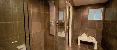 Un baño moderno con ducha de vidrio, un banco con toallas y un espejo con ventana.