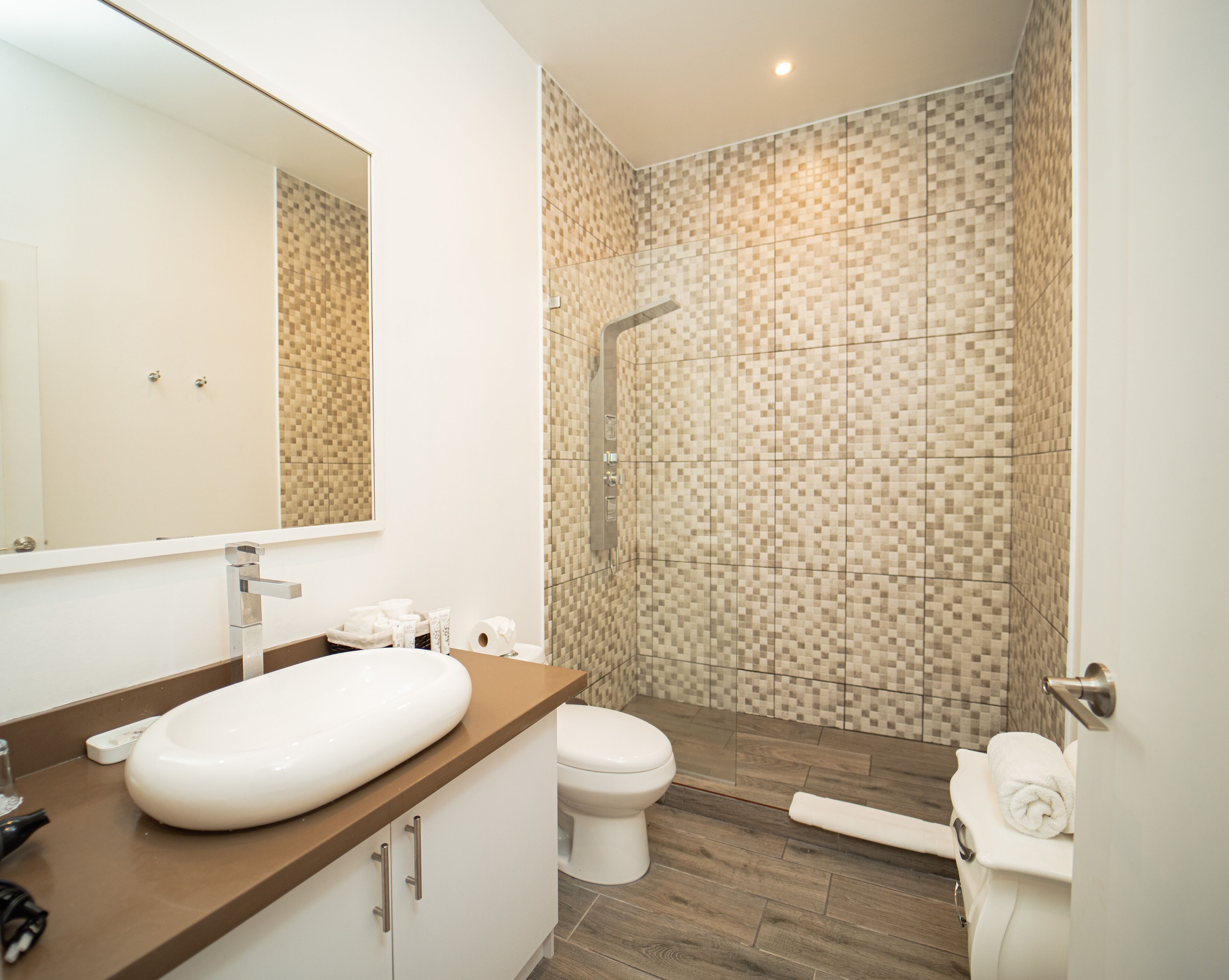 A modern bathroom with a large mirror, a white sink, a toilet, and a shower area with mosaic tiles.