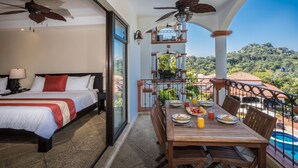 Een hotelkamer met balkon, bed, ontbijt aan een eettafel en uitzicht op het zwembad.