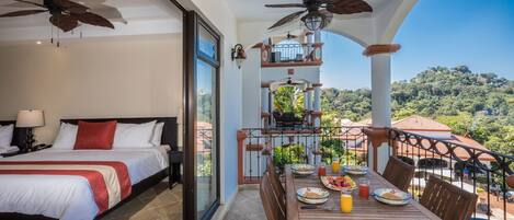 A hotel room with a balcony, a bed, a dining table with breakfast, and a pool view.