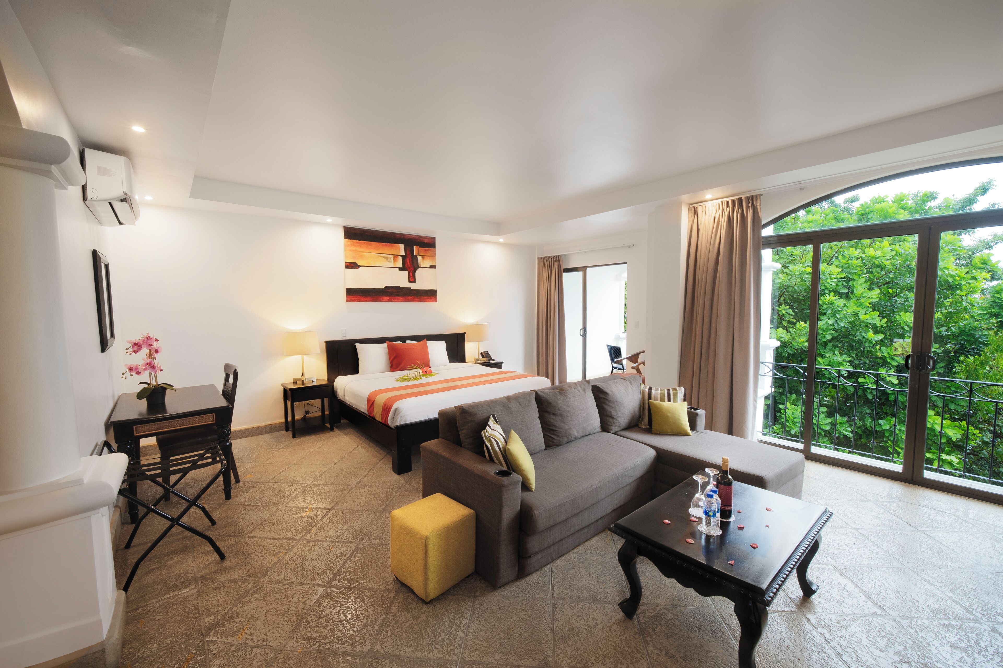 Una habitación de hotel con cama, sofá, mesa de comedor y balcón con vistas.