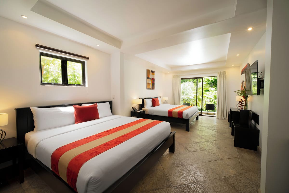 A hotel room with two beds, a sitting area, and a large window with a view of greenery.