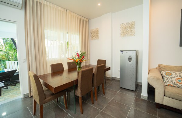 A dining area with a wooden table and chairs, a refrigerator, and a sofa with a patterned cushion.