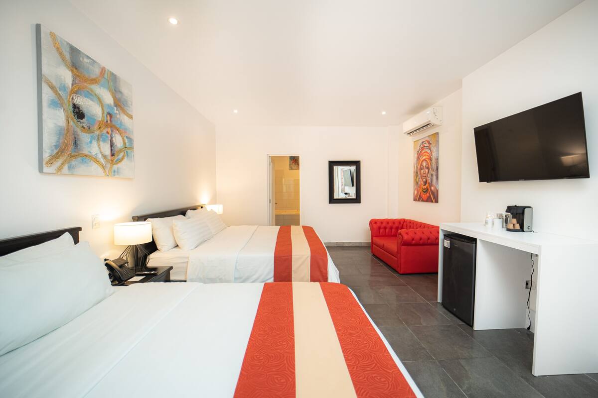 A hotel room with two beds, a red sofa, a TV, and a kitchenette.