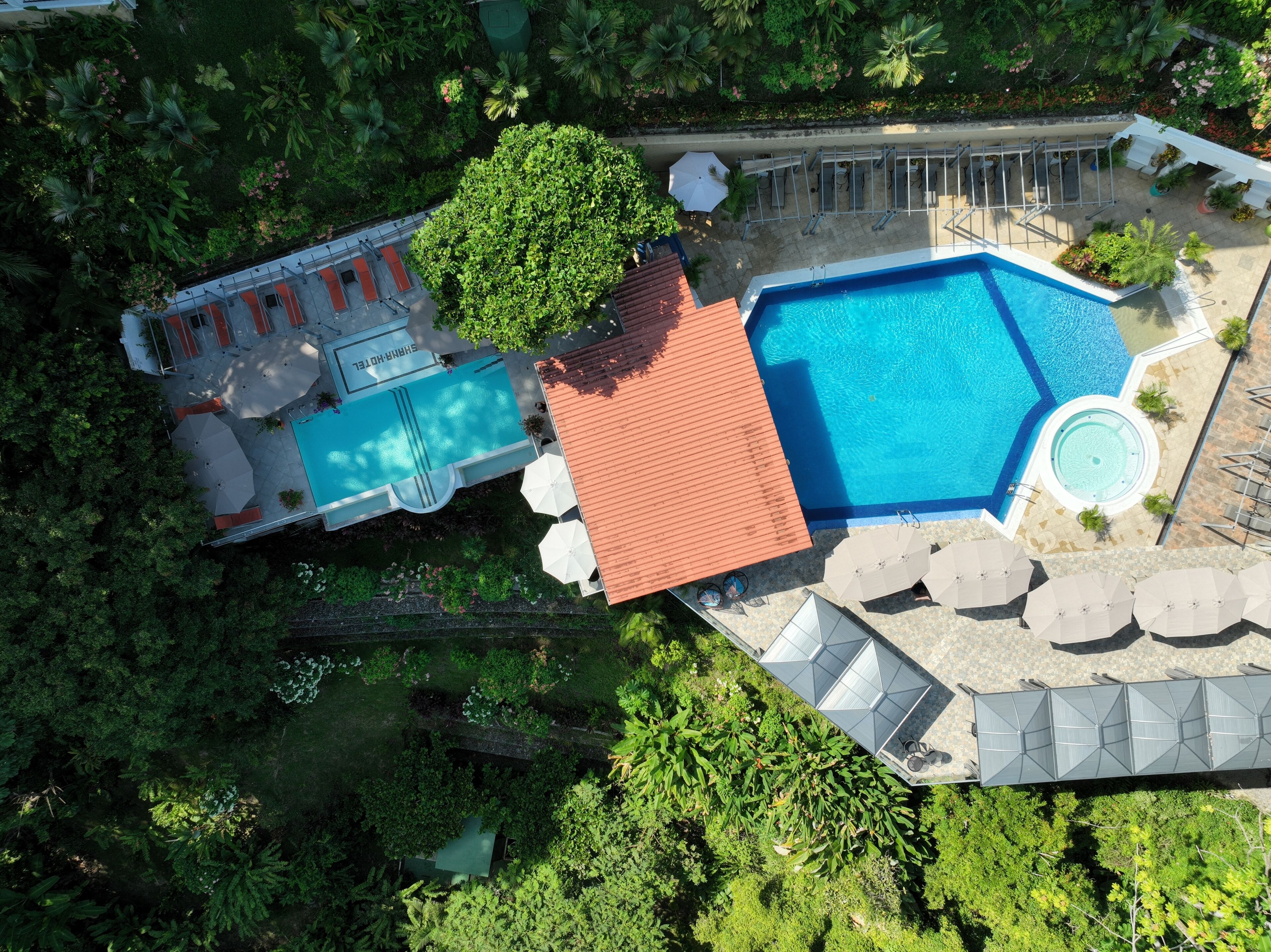 Luftaufnahme eines Resorts mit einem großen Swimmingpool, Liegestühlen und einer überdachten Sitzgelegenheit.