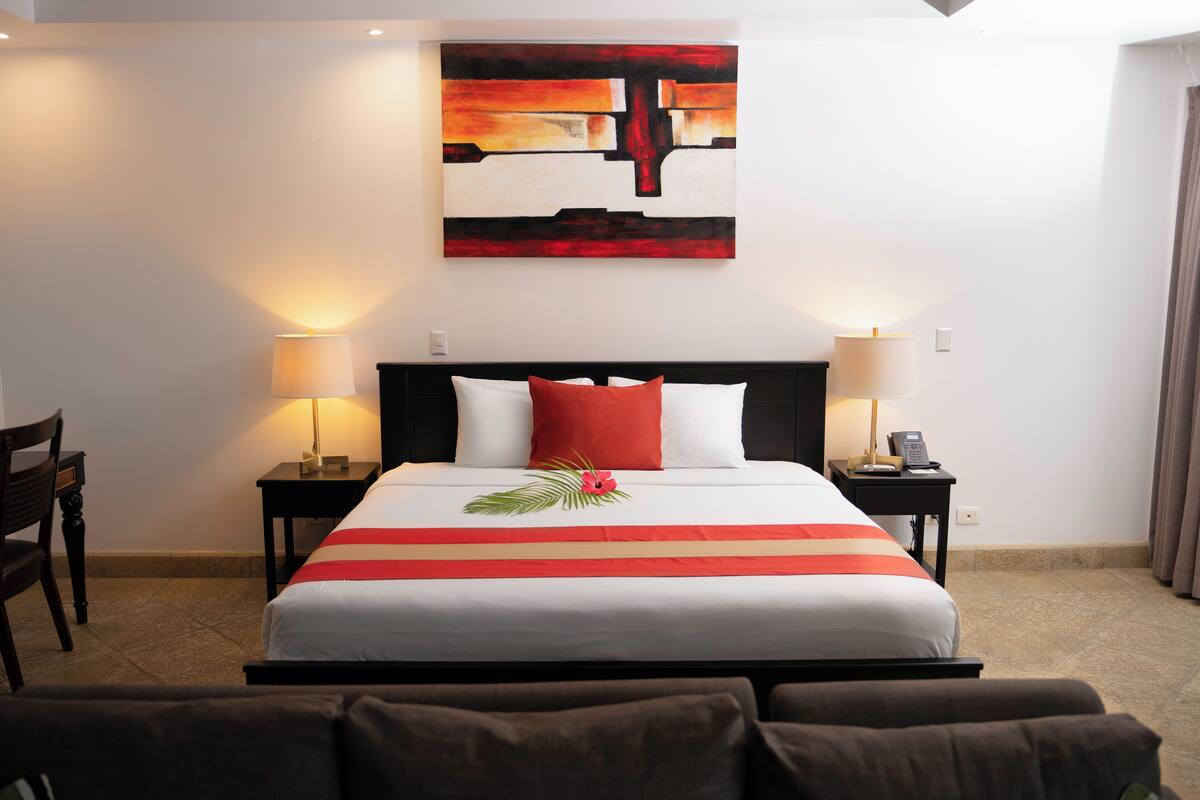 A hotel room with a large bed, two bedside tables with lamps, a modern abstract painting on the wall, and a floral decoration on the bed.