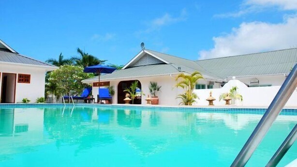 Una piscina con sillones y sombrillas, rodeada de edificios con diseño tropical.
