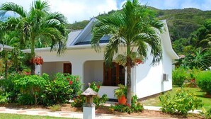 Una casa blanca con techo inclinado, rodeada de abundante vegetación y palmeras.