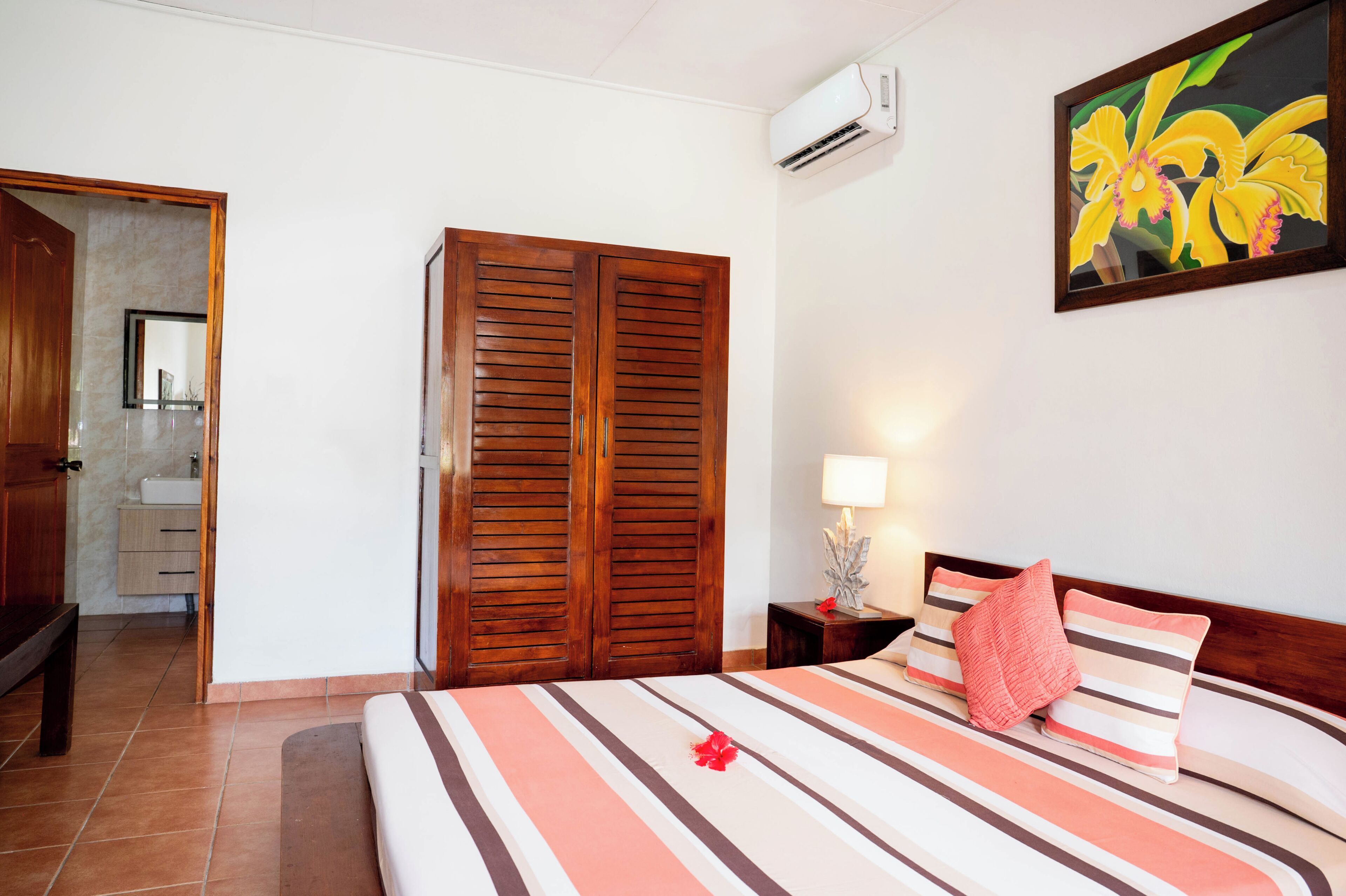 A hotel room with a bed, wooden wardrobe, bathroom, and an air conditioning unit.