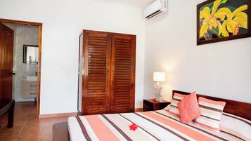A hotel room with a bed, wooden wardrobe, bathroom, and an air conditioning unit.